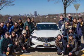 Students pose in front of the Acura car with the City of Pittsburgh in the background