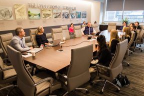Students and employees of JLL gather around the conference room table for a session.