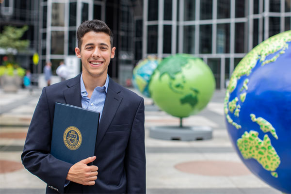 A smiling male student standing next to a large globe at Market Square in Pittsburgh