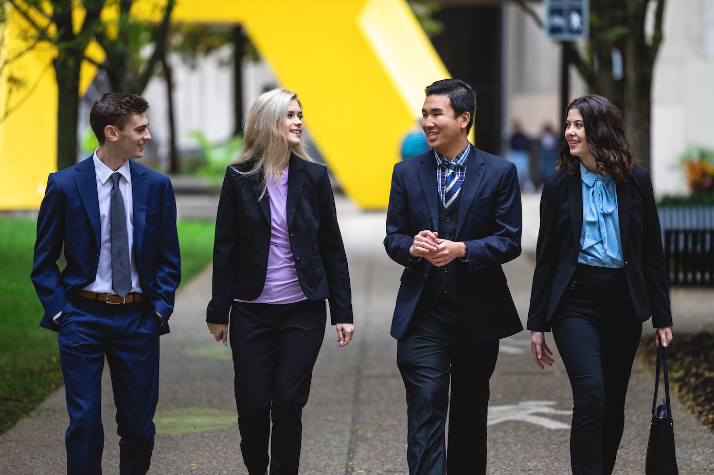 Four undergraduate students in business suits walking through campus.